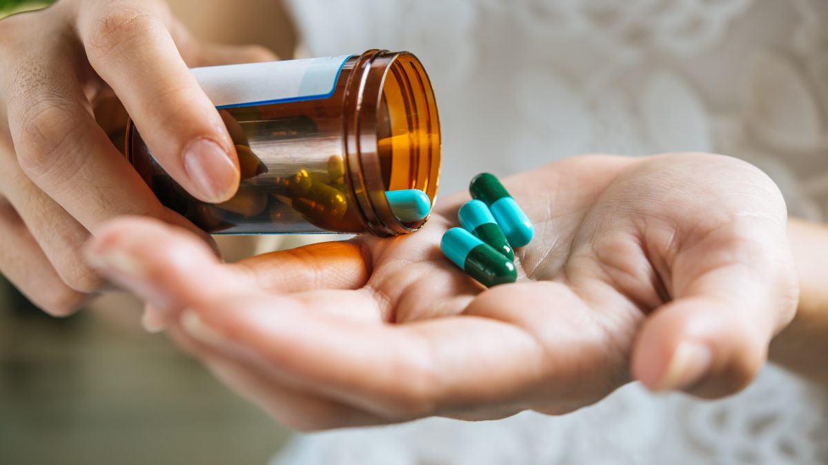 woman-s-hand-pours-medicine-pills-out-bottle-1200×675