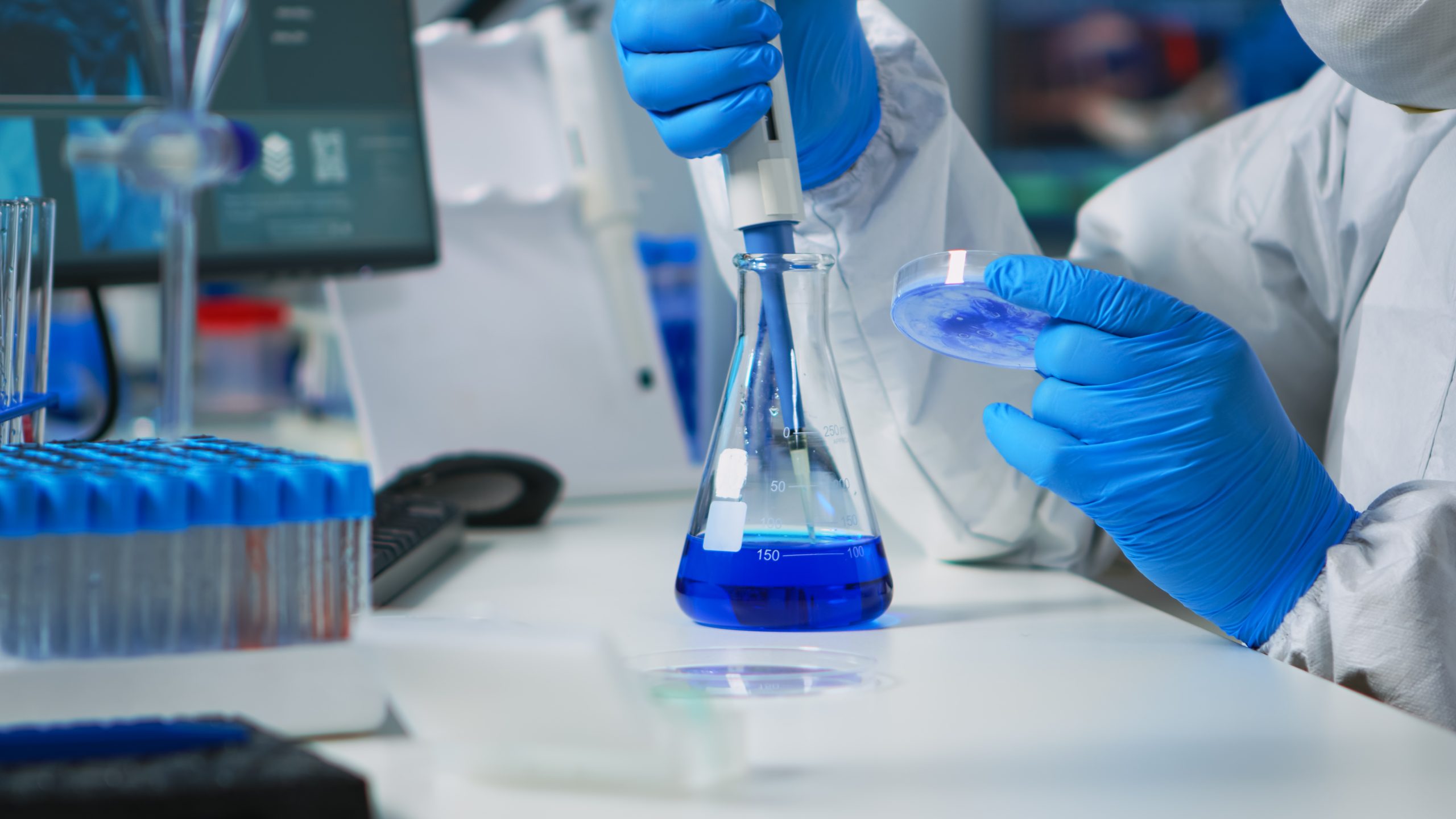 Doctor in ppe suit using pipette with microtiter plate and petri dish